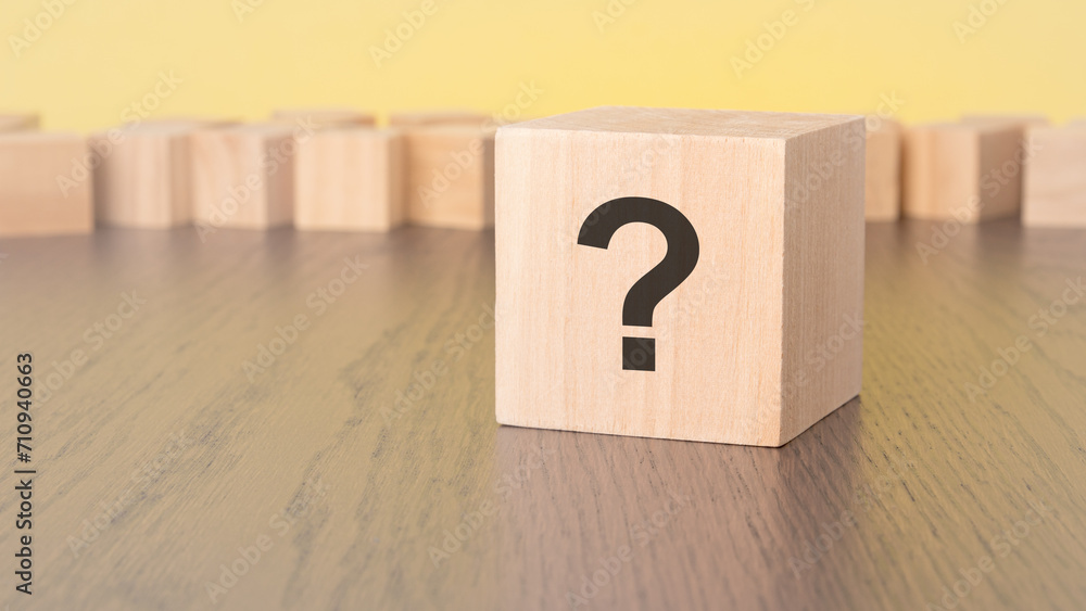 question mark written on wooden block lying on brown table, business and education concept. yellow background