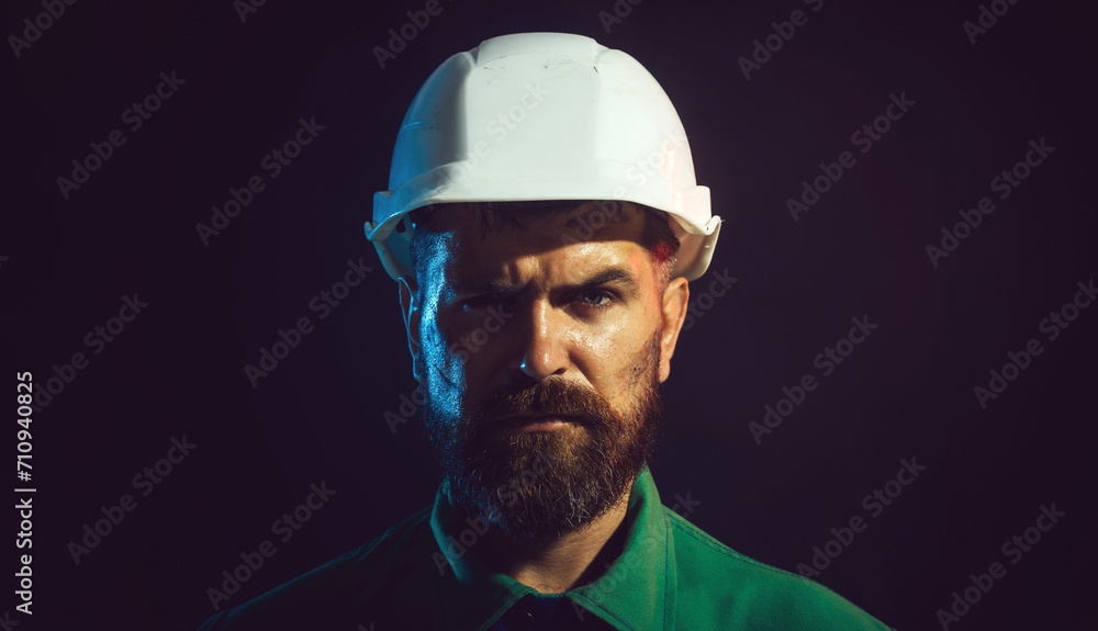 Closeup portrait of bearded man in protective helmet. Serious mechanical worker, foreman or repairman in construction hard hat. Male builder, architect or engineer in white hardhat and safety uniform.