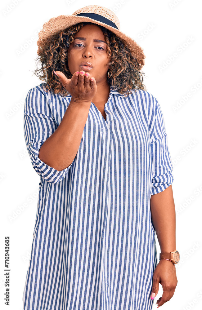 Young african american plus size woman wearing summer hat looking at the camera blowing a kiss with hand on air being lovely and sexy. love expression. Young african american plus size woman wearing summer hat looking at the camera blowing a kiss with hand on air being lovely and sexy. love expression.
