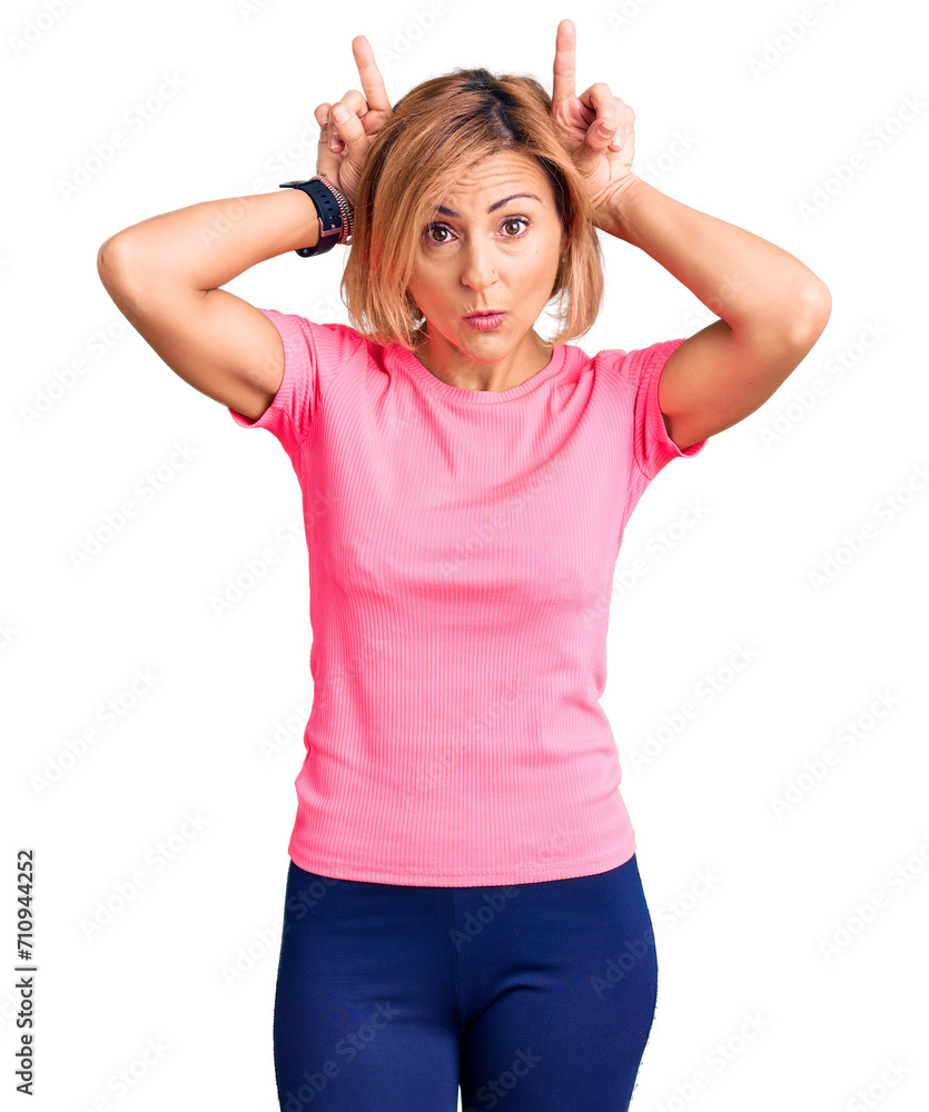 Young blonde woman wearing sportswear doing funny gesture with finger over head as bull horns Young blonde woman wearing sportswear doing funny gesture with finger over head as bull horns