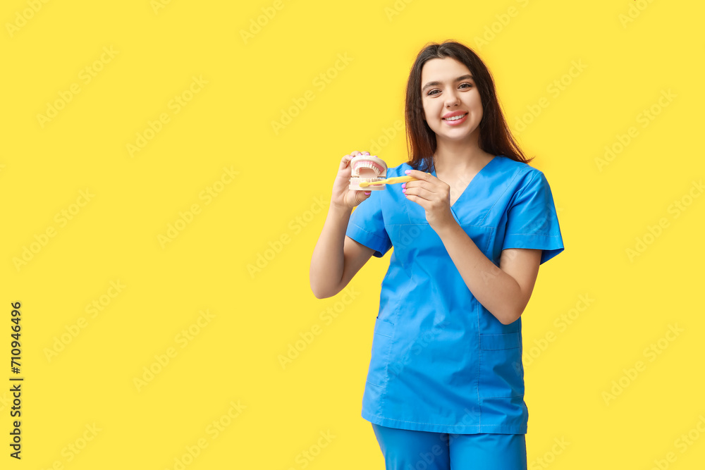 Female dentist with jaw model and toothbrush on yellow background. World Dentist Day Female dentist with jaw model and toothbrush on yellow background. World Dentist Day
