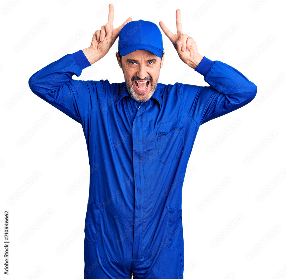 Middle age handsome man wearing mechanic uniform posing funny and crazy with fingers on head as bunny ears, smiling cheerful