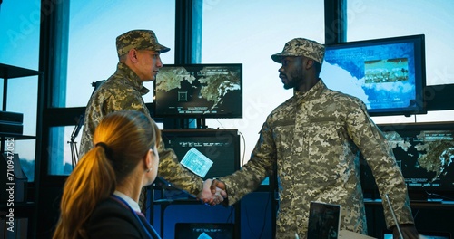 African american militarian man having speech at naval consultation in front of mixed-races staff. Caucasian male soldier coming in, shaking hands and joining meeting at table. photo