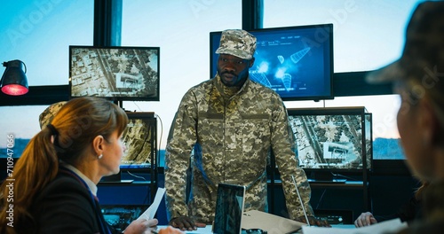 African American male head of militarian headquarters talking with report to Caucasian army staff while people studying and reading documents. Military training in office concept.