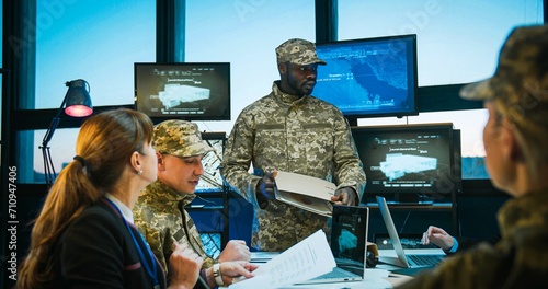 African American young military male general handing documents to Caucasian army staff at meeting. Conference on army studing and planning. Brainstorming of naval strategy. Troops studying. photo