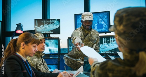 African American young man, head of headquarters coming in and handing documents with tasks to Caucasian troops workers. Metting about army studing and planning. Brainstorming of army operation. photo