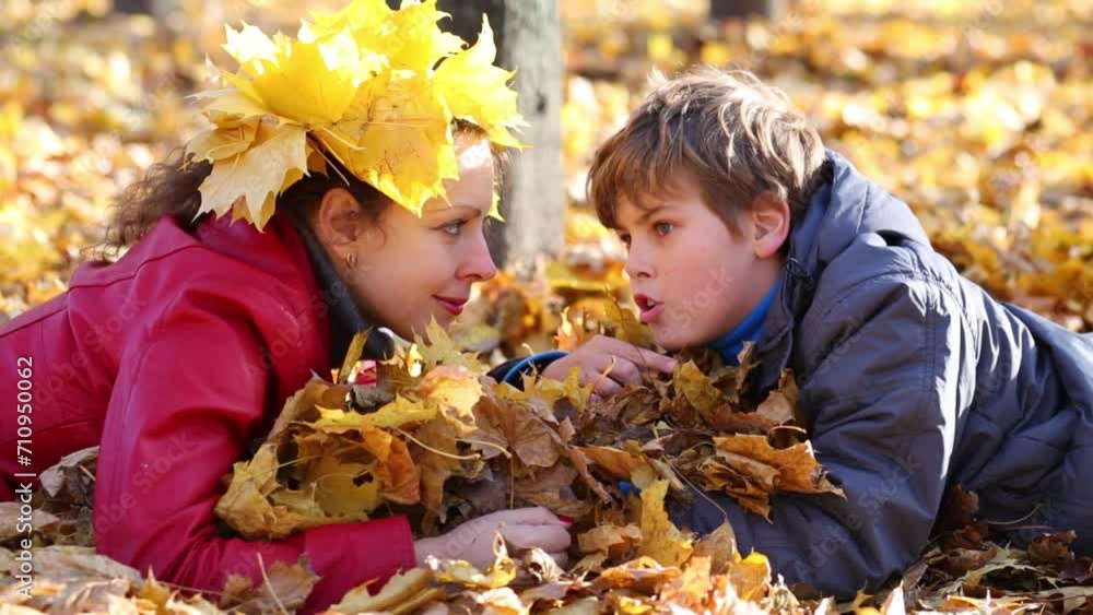 Mother and son lie on yellow leaves and talk in autumn park 