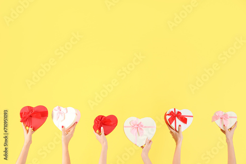 Female hands holding different heart-shaped gift boxes on yellow background. Valentine's Day celebration