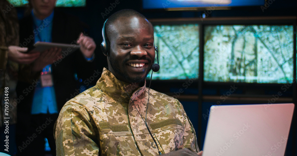 Portrait of African American military man in headset sitting at laptop computer in controlling center of army and smiling joyfully to camera. Male soldier in military office. Officer in dispatch room. Portrait of African American military man in headset sitting at laptop computer in controlling center of army and smiling joyfully to camera. Male soldier in military office. Officer in dispatch room.