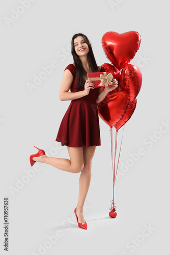 Beautiful young woman with heart-shaped air balloons and gift for Valentine's day on grey background © Pixel-Shot