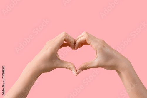 Female hands showing heart gesture on pink background. Valentine s Day celebration