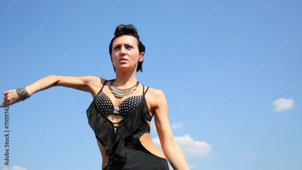 Slim woman in black costume dances at background of blue sky Slim woman in black costume dances at background of blue sky