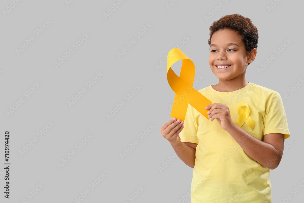 Cute little African-American boy with yellow ribbons on grey background. Childhood cancer awareness concept Cute little African-American boy with yellow ribbons on grey background. Childhood cancer awareness concept