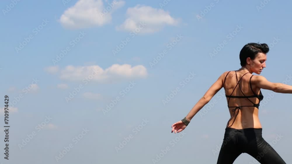 Young woman in black costume dances at background of blue sky Young woman in black costume dances at background of blue sky