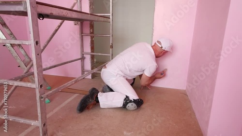 Worker in cap and white clothes paints wall in pink room photo