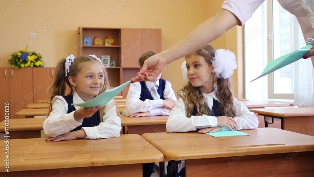 Two girls and boy sit in classroom and teacher gives notebooks Two girls and boy sit in classroom and teacher gives notebooks