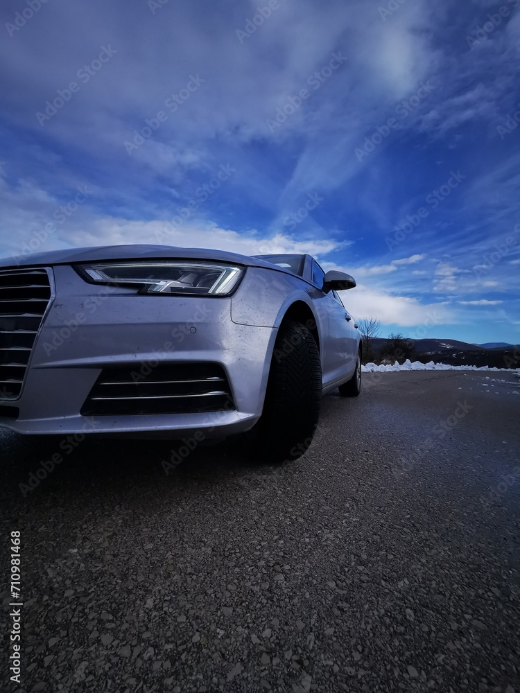 headlight of modern prestigious car on winter road under blue cloudy sky. Front lights with close-up detail