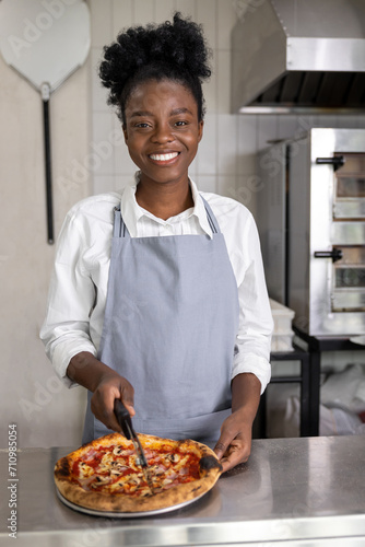 Smiling dark-skinned woman cutting pizza and looking contented
