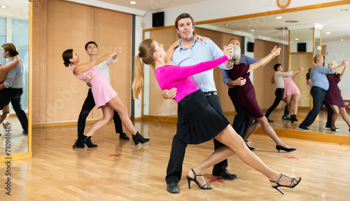 Smiling modern woman and man dancing slow ballroom dance during group class in choreography studio