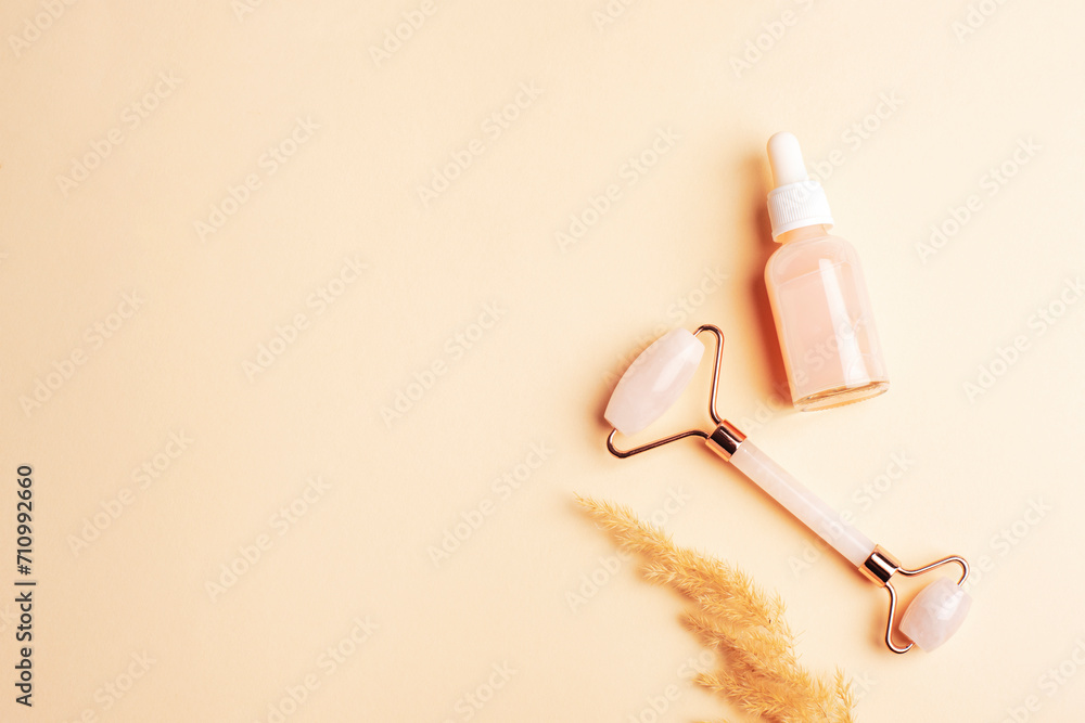 Pink serum bottle, rose quartz crystal facial roller and pampas grass on neutral beige background. Top view, flat lay, copy space Pink serum bottle, rose quartz crystal facial roller and pampas grass on neutral beige background. Top view, flat lay, copy space