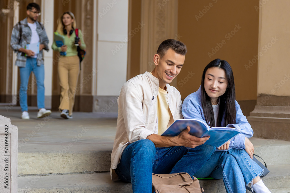 Two students sitting on school stairs reading book together. Two students sitting on school stairs reading book together.