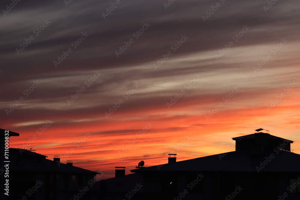 A dramatic sunset with radiant hues of orange and red streaking across the sky, silhouetting the rooftops of urban buildings. A dramatic sunset with radiant hues of orange and red streaking across the sky, silhouetting the rooftops of urban buildings.