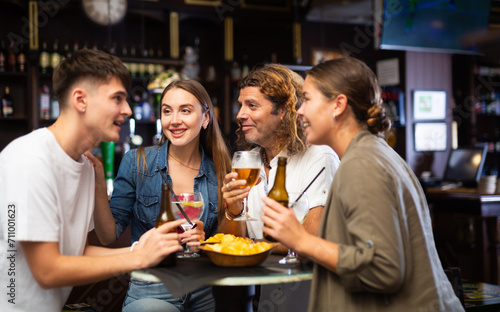 Cheerful men and women drinking beer and eating crisps  laughing and spending time together in a bar