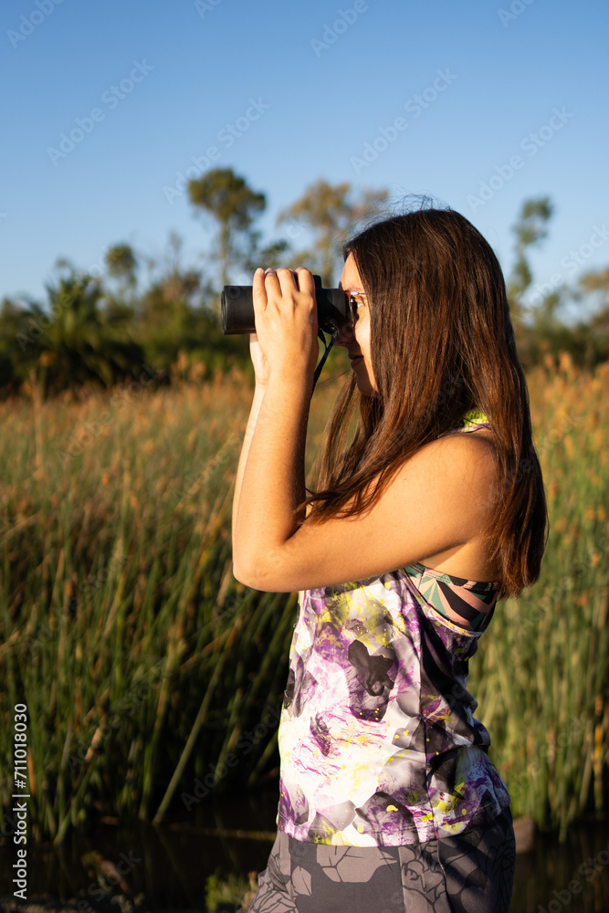 Young Latina woman looking through her binoculars outdoors on a sunny day. Young Latina woman looking through her binoculars outdoors on a sunny day.