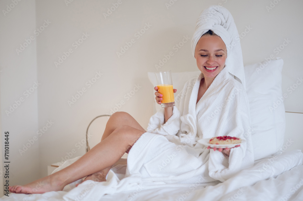 Cute young woman in bath robe having breakfast and feeling enjoyed Cute young woman in bath robe having breakfast and feeling enjoyed
