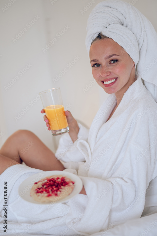 Cute young woman in bath robe having breakfast and feeling enjoyed Cute young woman in bath robe having breakfast and feeling enjoyed