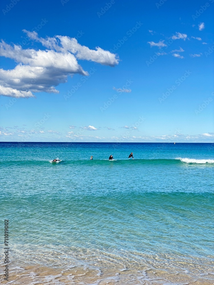 Surfers practicing catching a wave in the turquoise-blue ocean. Surf lesson. A day at the beach on a sunny day. Surfers practicing catching a wave in the turquoise-blue ocean. Surf lesson. A day at the beach on a sunny day.