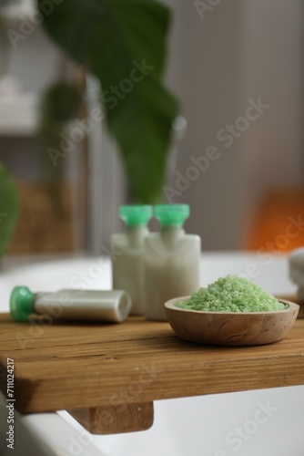 Wooden tray with cosmetic products and sea salt on bath tub in bathroom, closeup