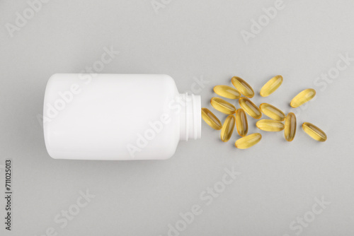 Bottle and vitamin capsules on light grey background, top view