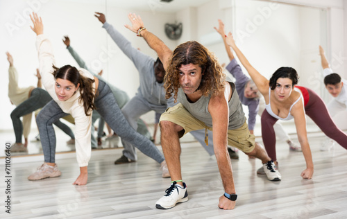 Focused adult man doing stretching workout with group of people before dance training in choreography class