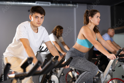 Men and woman taking indoor cycling class at fitness center, doing cardio riding bike