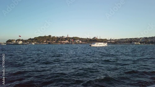 Evening, cinematic slow-mo, a mesmerizing view of Sarayburnu from a ferry on the Golden Horn in Istanbul. The shot showcases a ferry sailing left to right, Hagia Sophia and cityscape in background. photo