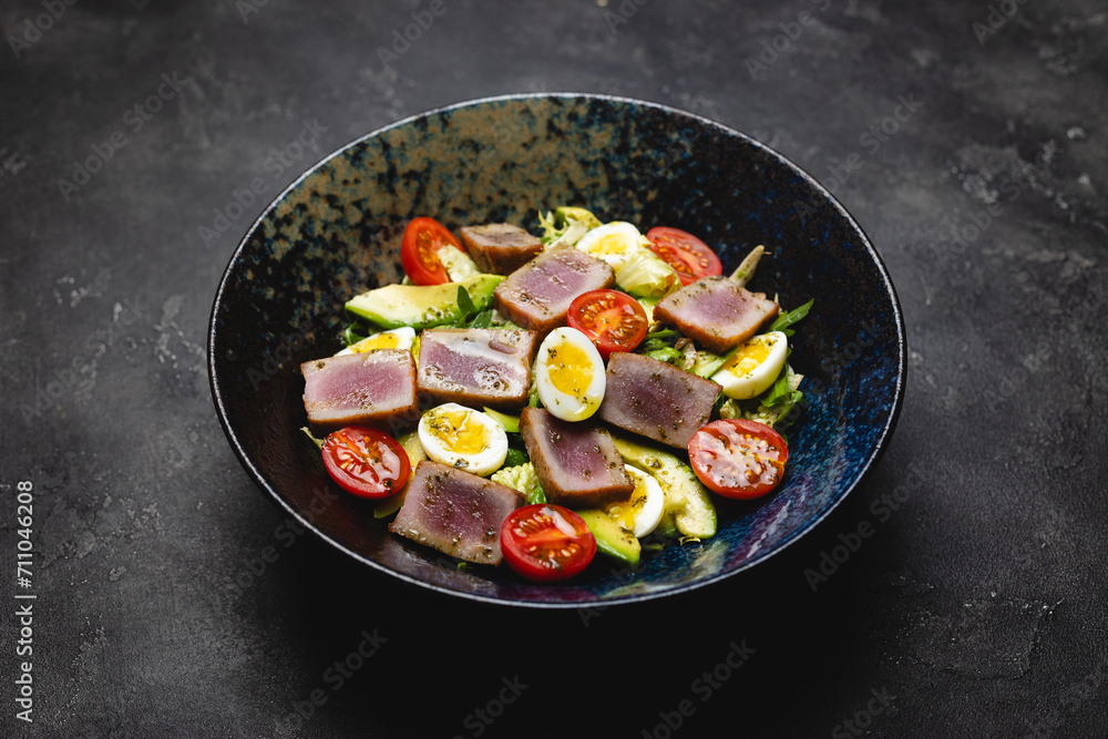 Appetizing salad nicoise in a deep beautiful plate on a dark background