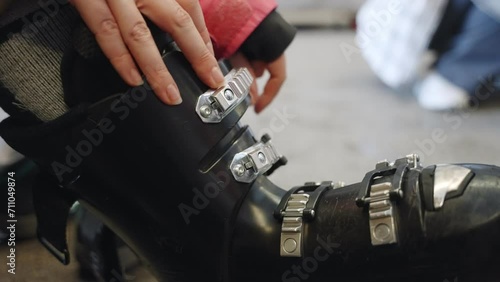 Close up on hand locking ski boot buckles in locker room in ski resort. Winter ski vacation - woman wearing special ski boots closing latches before going out for ski activity in snowy mountain photo