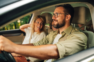 Father holding a wheel and driving a car with his family traveling together