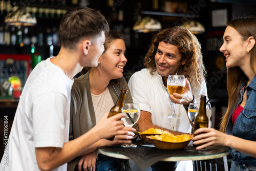 Cheerful young adult friends having fun together in vintage pub, talking and drinking beer at table