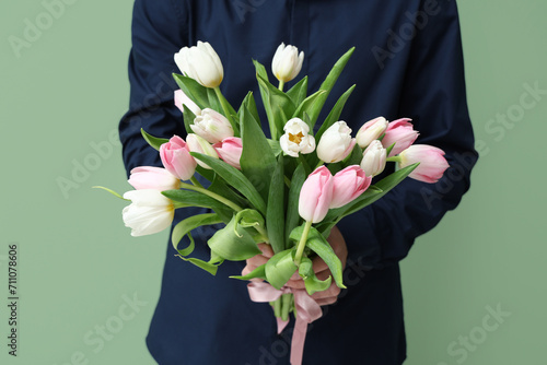 Young man with bouquet of beautiful tulips on green background. International Women's Day