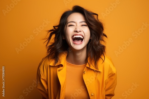 Laughing woman with brown hair wearing a yellow shirt and jacket