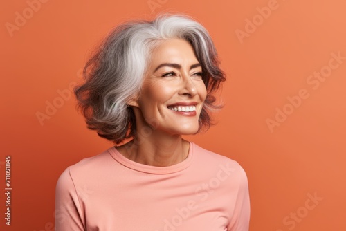 Portrait of happy mature woman with grey hair on orange background.