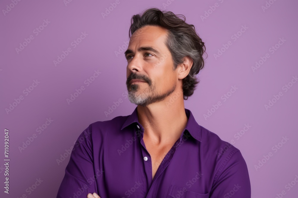 Portrait of a handsome mature man in purple shirt looking away while standing against purple background