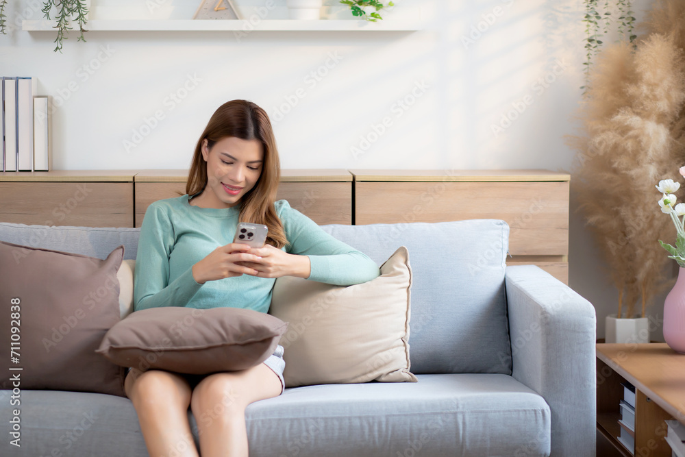 Happiness young asian woman smile sitting on sofa using smart phone with cozy in living room at home, happy woman on couch watching social media on smartphone with relax, lifestyles concept. Happiness young asian woman smile sitting on sofa using smart phone with cozy in living room at home, happy woman on couch watching social media on smartphone with relax, lifestyles concept.