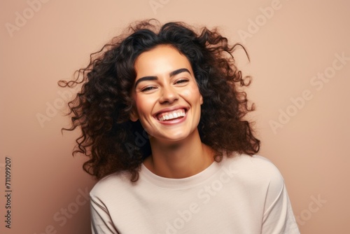 Portrait of a beautiful smiling young woman with curly hair on a beige background
