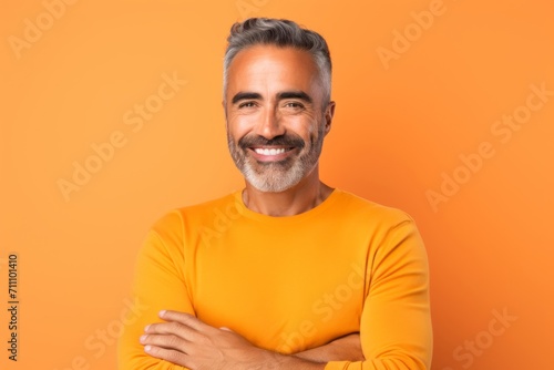 Portrait of happy mature man with crossed arms over orange background. © Iigo