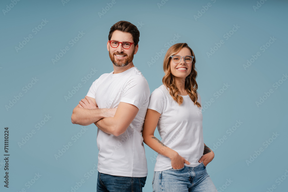 Portrait of successful smiling man and woman wearing white t shirt and stylish glasses isolated on blue background. Happy attractive fashion models with arms crossed posing for pictures in studio Portrait of successful smiling man and woman wearing white t shirt and stylish glasses isolated on blue background. Happy attractive fashion models with arms crossed posing for pictures in studio
