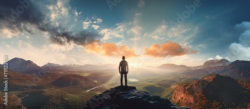 Man standing on a mountaintop overlooking a valley at sunset photo