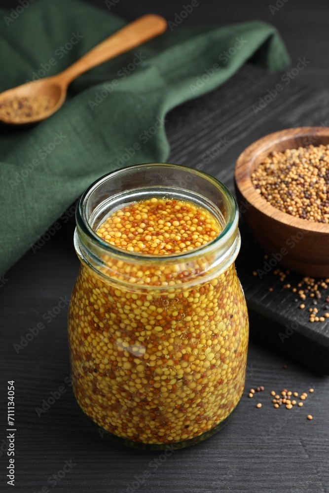 Whole grain mustard in jar and dry seeds on black wooden table Whole grain mustard in jar and dry seeds on black wooden table